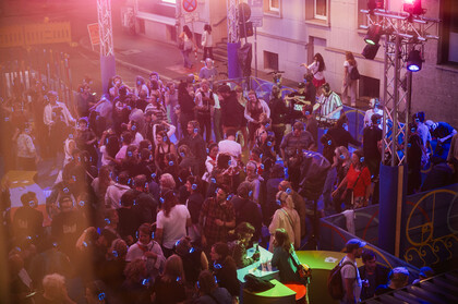 Eine Menschenmenge im Festivalzentrum mit blau leuchtenden Kopfhörern aus der Vogelperspektive betrachtet.