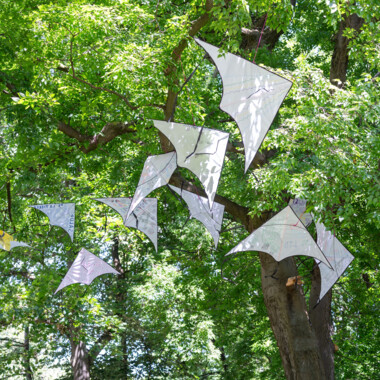 Ein Foto von der Installation "Vituka – Towards an Education of the Senses: Weiße, unterschiedlich gestaltete Drachen hängen an einem Baum.