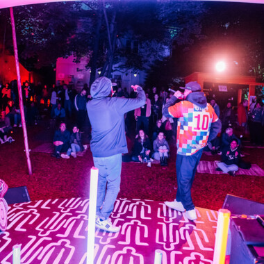 Photo from the open-air concert: Eskina Qom and a DJ from the side, with the audience sitting and standing in front of them.
