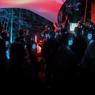Viele Personen mit blau leuchtenden Kopfhörern tanzend im Festivalzentrum.