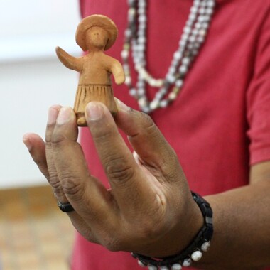 One hand holds a ceramic figure to the camera.