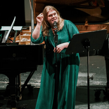 Gisa Flake in einem grünen Kleid vor einem Mikrofon stehend.